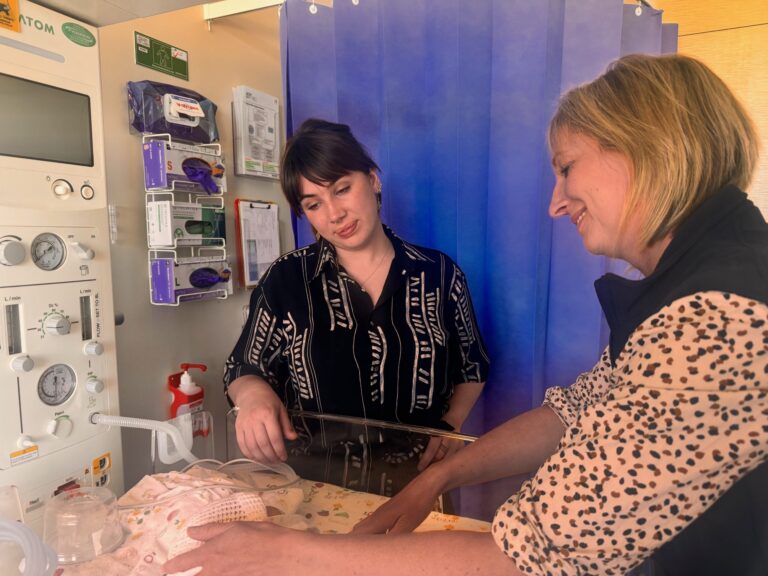 two midwives looking into a neonatal cot with loving looks on their faces