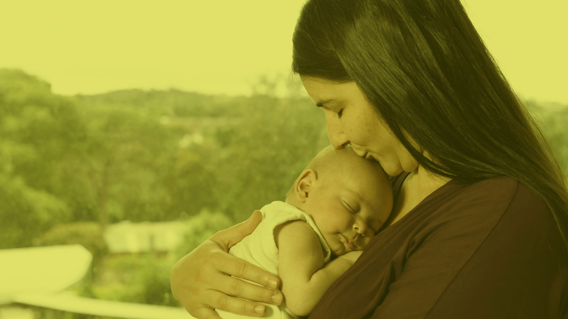 woman holding a newborn baby and kissing them on the head.