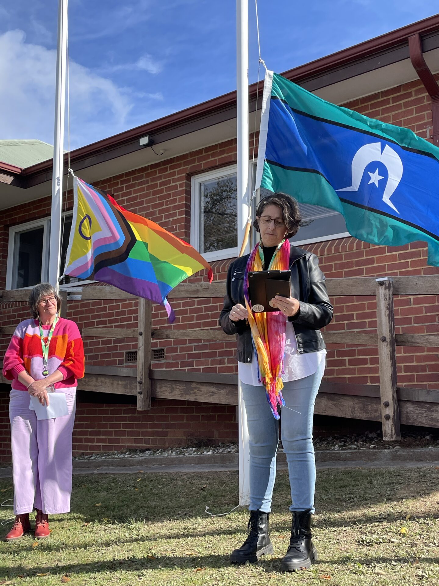 Photo of Auntie Kerri Douglas and CEO Sue Race standing in front of the Intersex Progress Flag at Dhelkaya Health