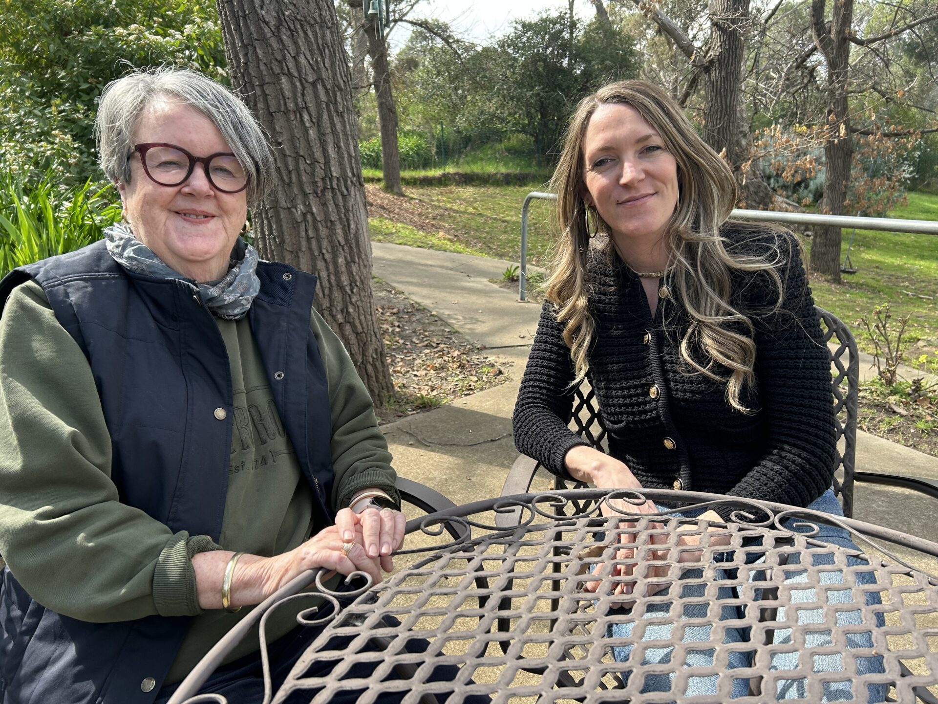 Two women in casual dress sitting at an outdoor setting in a garden