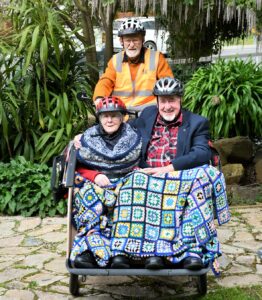 Trishaw Pilot riding trishaw through park with two passengers tucked under a crocheted rug