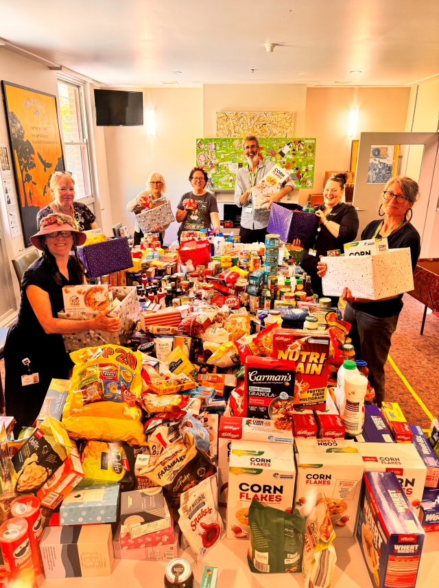 Seven Dhelkaya Health staff standing around a large table filled with food to be donated to the Christmas Tree Project