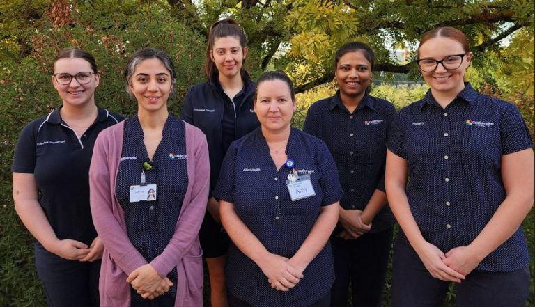 Six members of the Dhelkaya HEalth Falls Team standing in front of some green foliage.