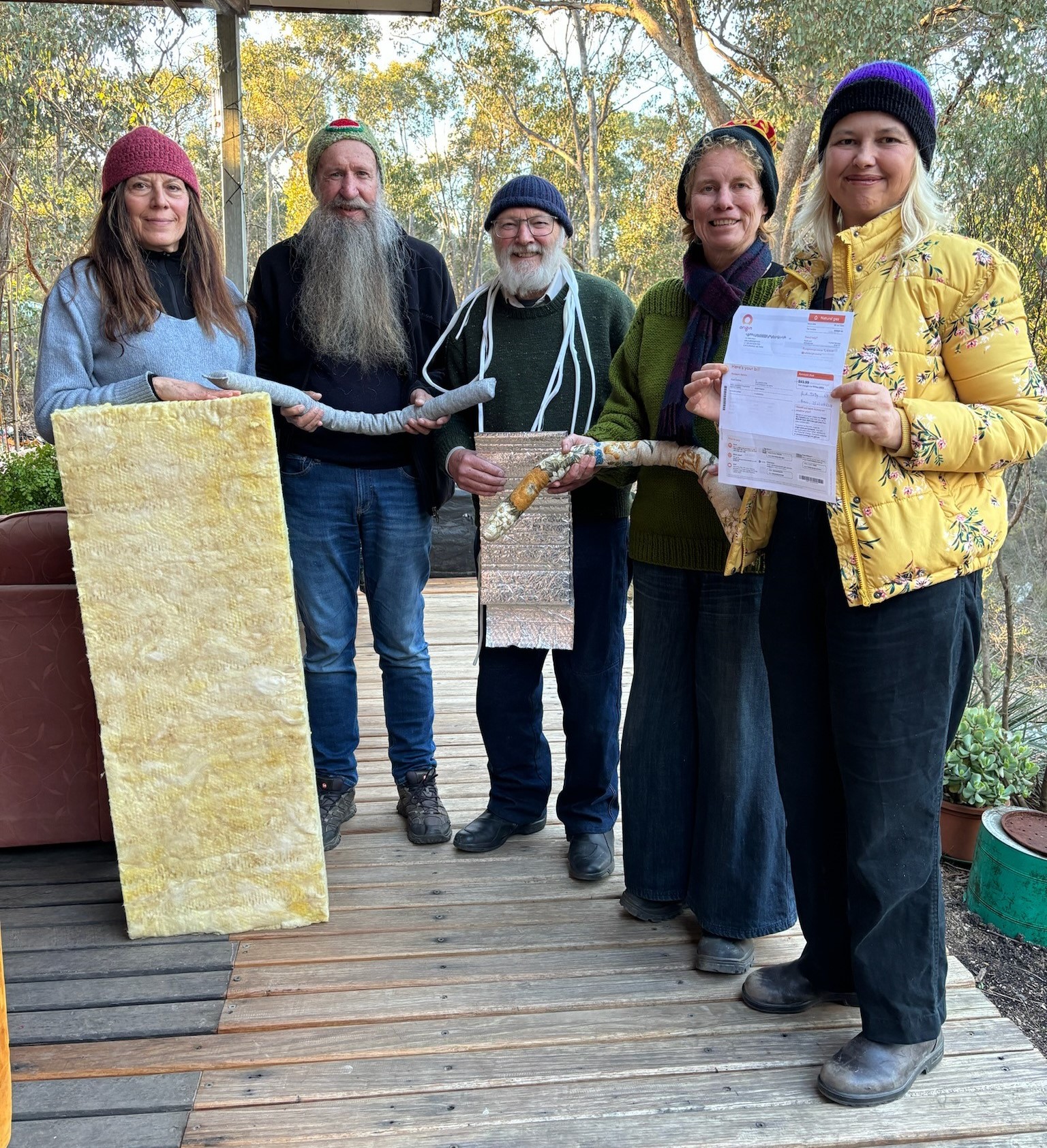 five adults standing outside, wearing warm coats (names listed in the caption) displaying items like insulation bats and draught stoppers that would help a rental be more energy efficient.