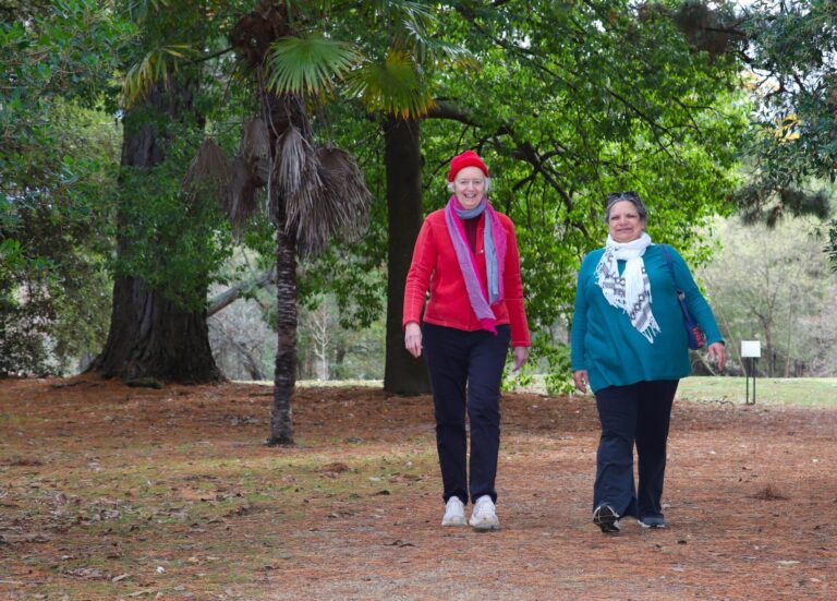 Two women dressed in warm clothes and smiling, walking through a botanic gardens