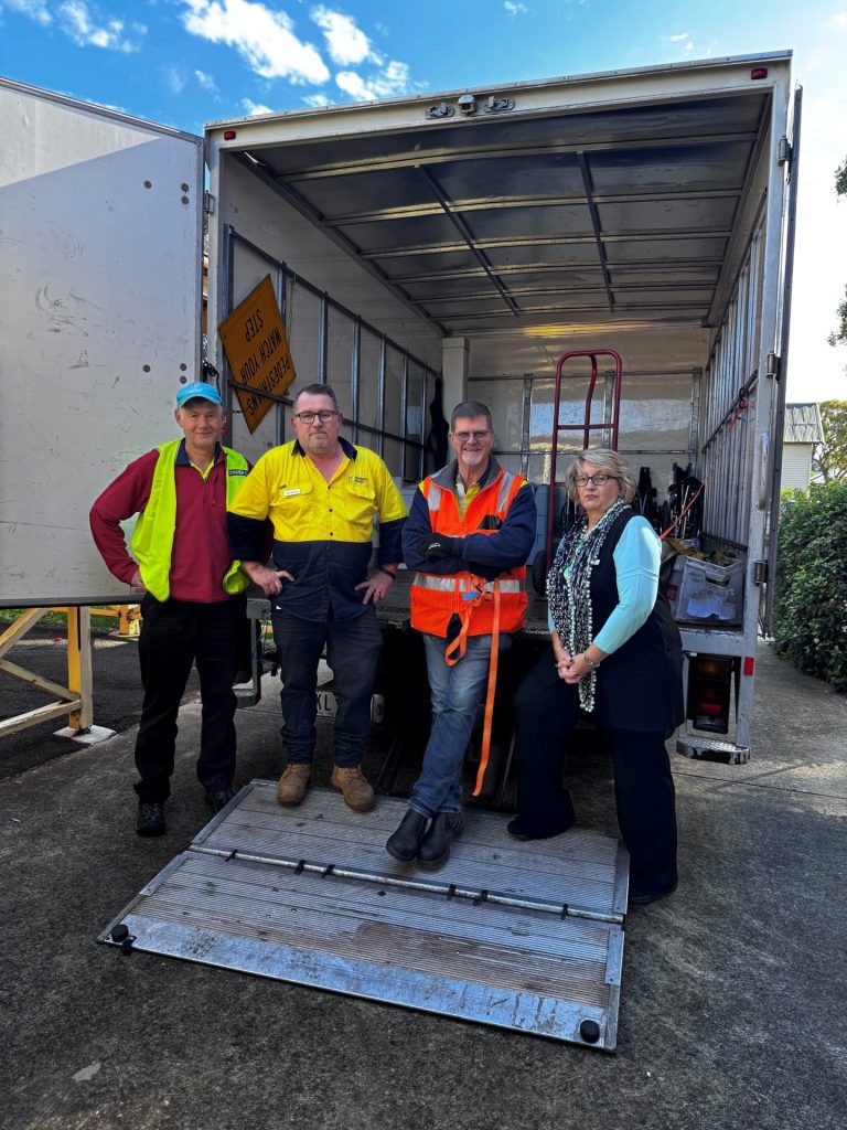 3 men in high-vis shirts and our female Nurse Unit Manager standing in front of an empty truck